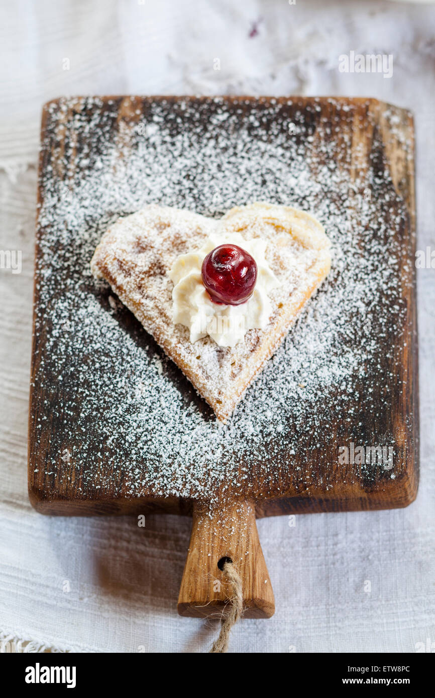 Gaufres en forme de cœur avec de la crème fouettée et de cerises on cutting board Banque D'Images