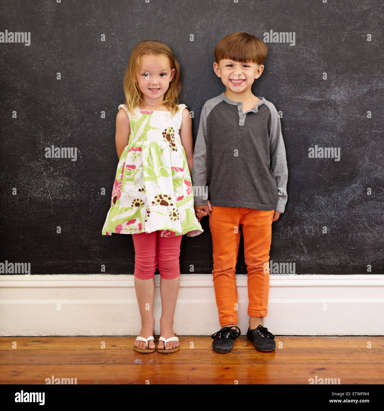 Toute la longueur de balle deux jeunes enfants se tenant ensemble contre un tableau noir. Petit garçon et petite fille à l'accueil looking at camera Banque D'Images