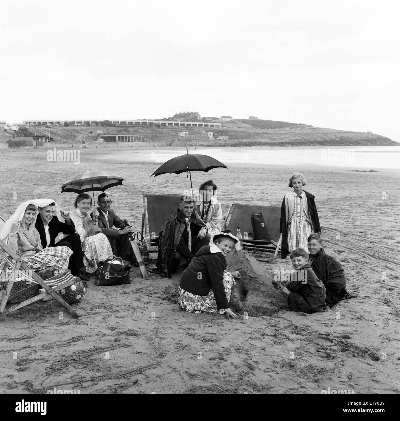 Les familles à l'abri de la pluie sous des couvertures et des parasols sur la plage du Barry Island, Vale of Glamorgan, Pays de Galles. 14 juillet 1960. Banque D'Images