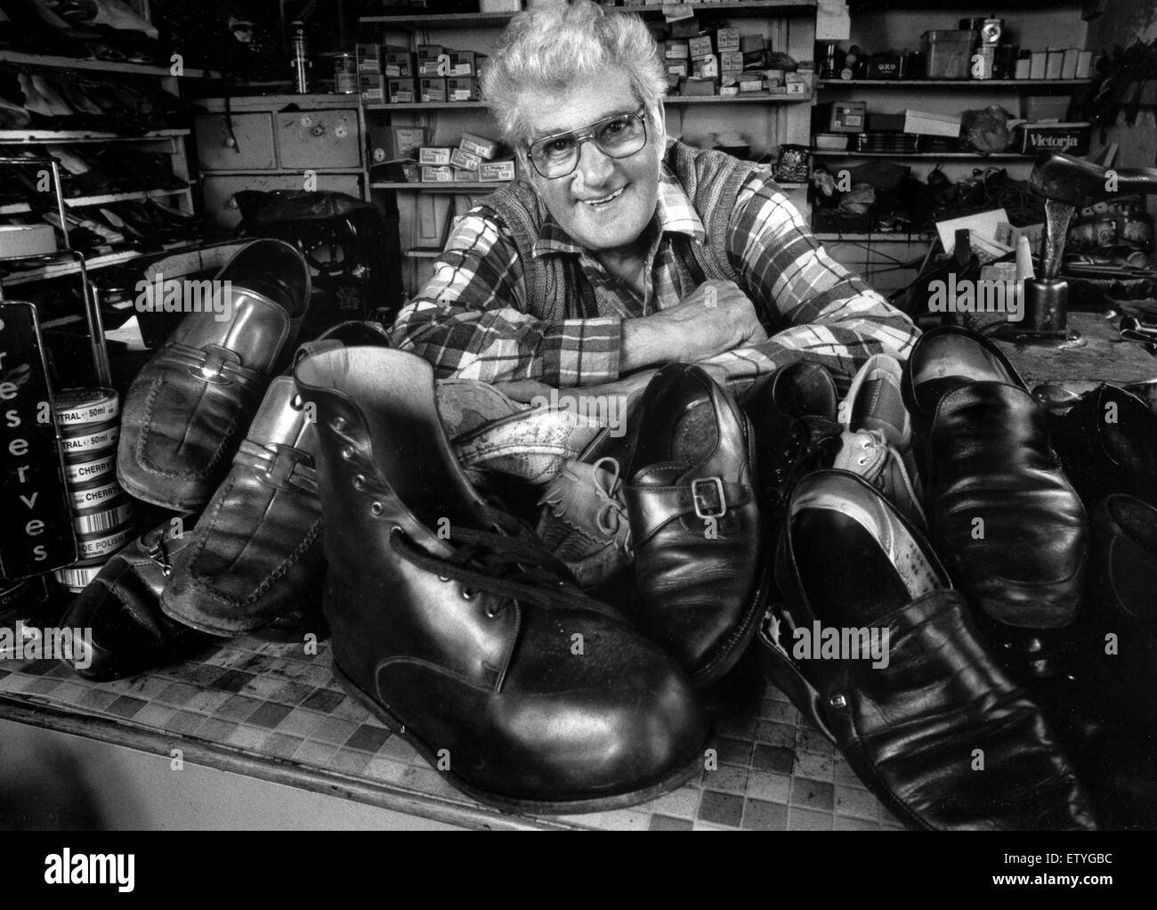 Cordonnier entouré de vieux souliers et bottes dans son atelier de réparation de chaussures 1984 Brighton Banque D'Images