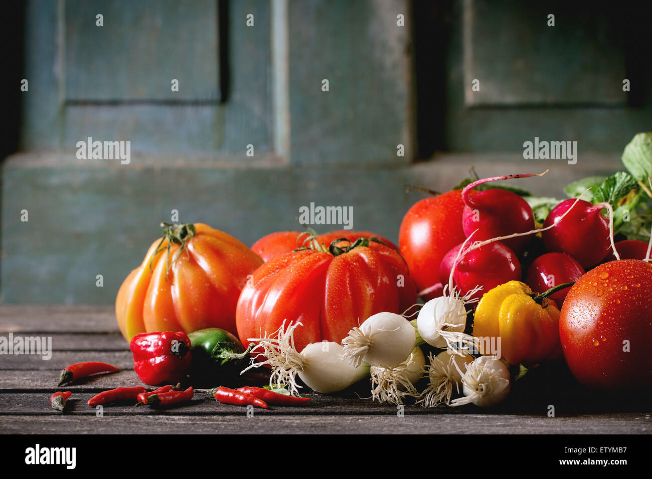 Tas de légumes colorés frais mûrs tomates, piments, l'oignon vert et bande de radis plus vieille table en bois. La rouille noire Banque D'Images