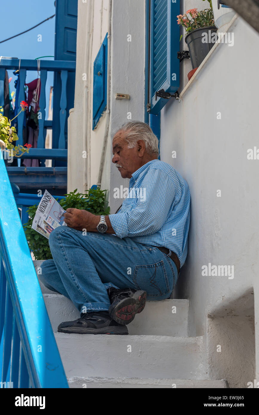 Greek man reading newspaper sur les marches d'une maison traditionnelle blanchie à la Méditerranée avec boiseries bleu Banque D'Images