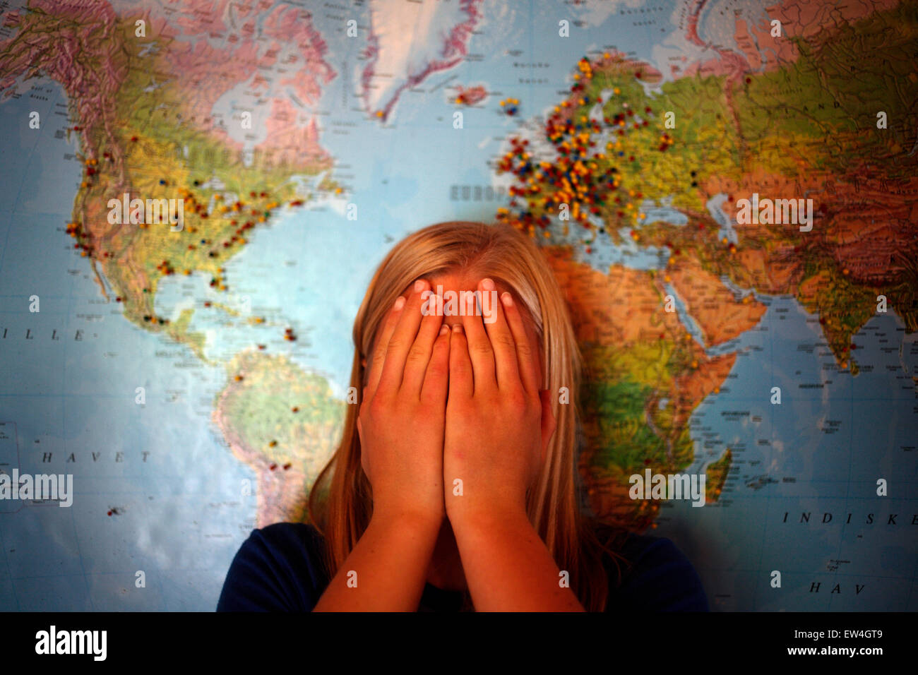 Une jeune femelle Norvégienne se tient devant une carte du monde axée sur l'Europe avec ses mains sur son visage. Banque D'Images