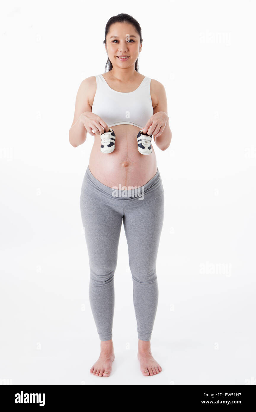 Femme enceinte tenant une paire de chaussures de bébé et souriant à la caméra, Banque D'Images