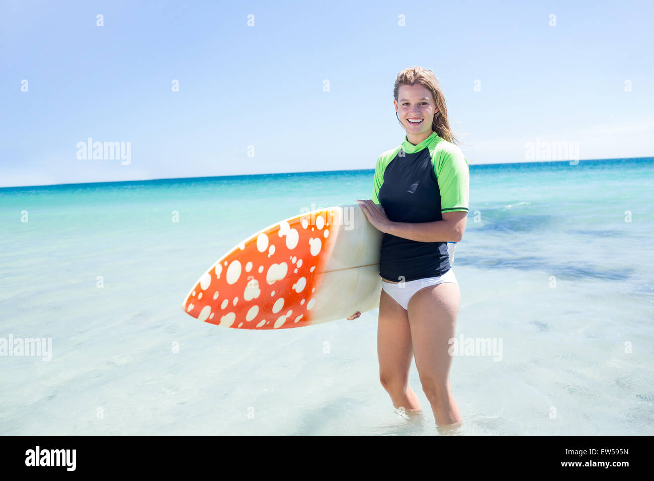 Femme blonde fit debout dans l'eau et la tenue de surf Banque D'Images