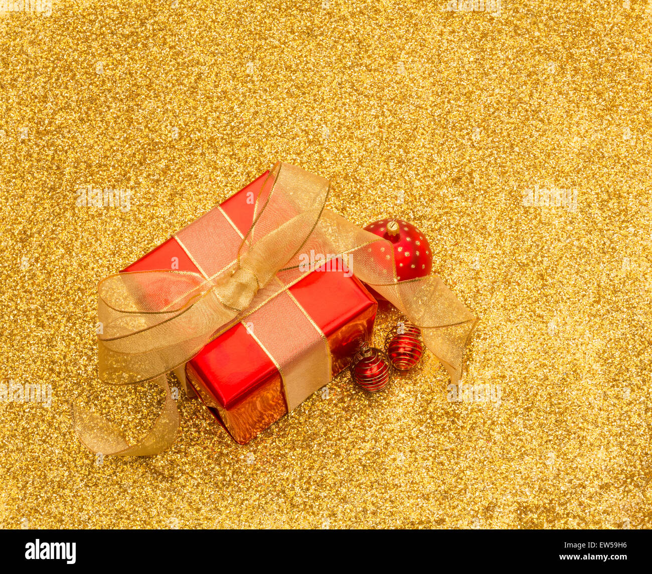 Boîte cadeau rouge et or avec boules ruban sur une gold glitter background with copy space Banque D'Images