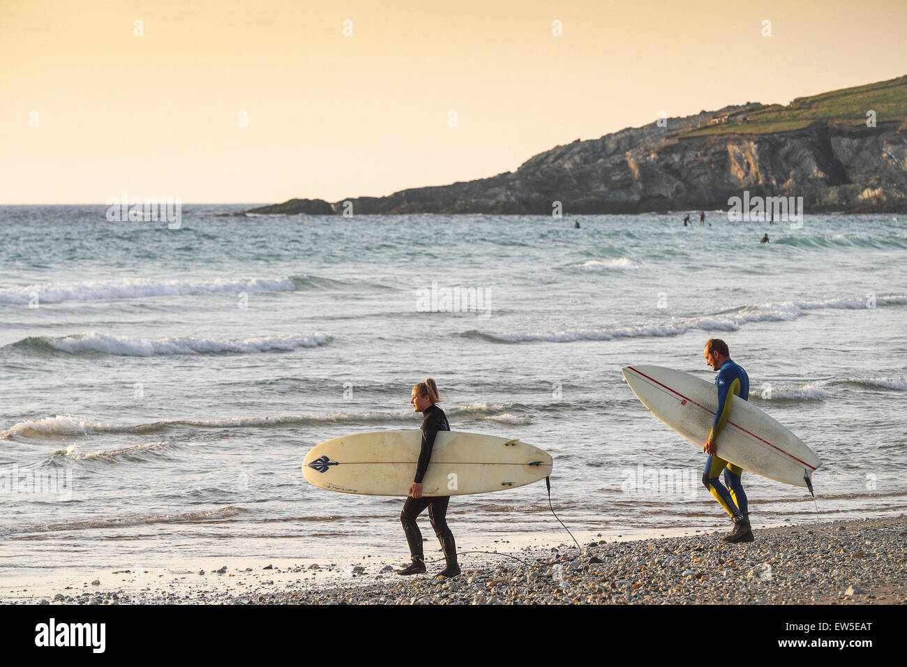Deux surfeurs de marcher dans la mer alors que le soleil se couche sur la plage de Fistral, Newquay, Cornwall. UK. Banque D'Images