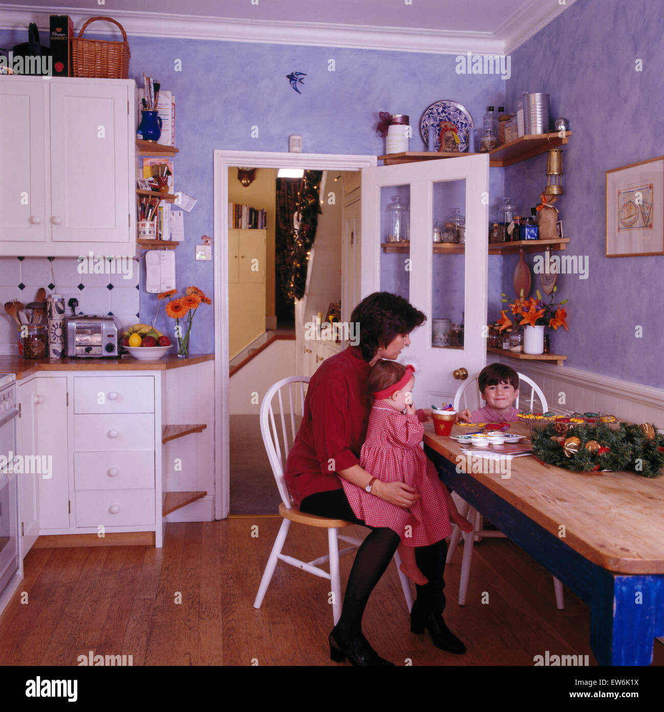Mère avec de petits fils et fille assis à table dans une cuisine 80 mauve Banque D'Images