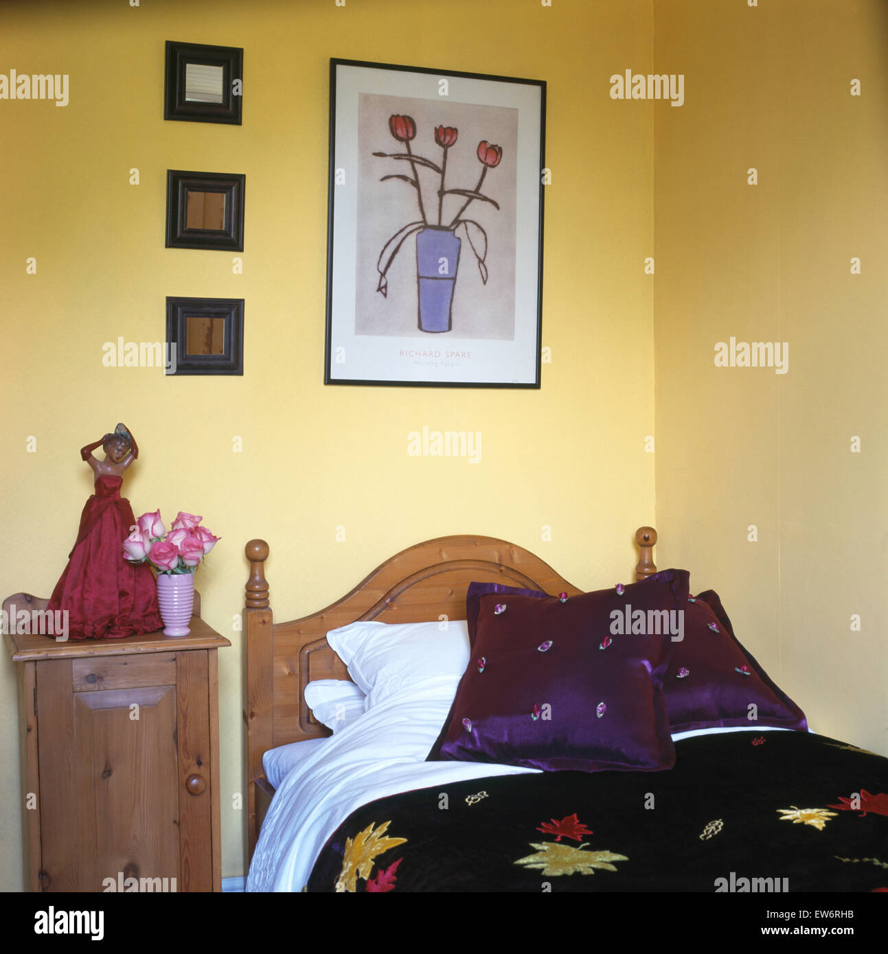 Photos sur mur au-dessus de lit en pin avec coussins violets en jaune pâle 90 chambre avec une trentaine de figurine de chevet Banque D'Images