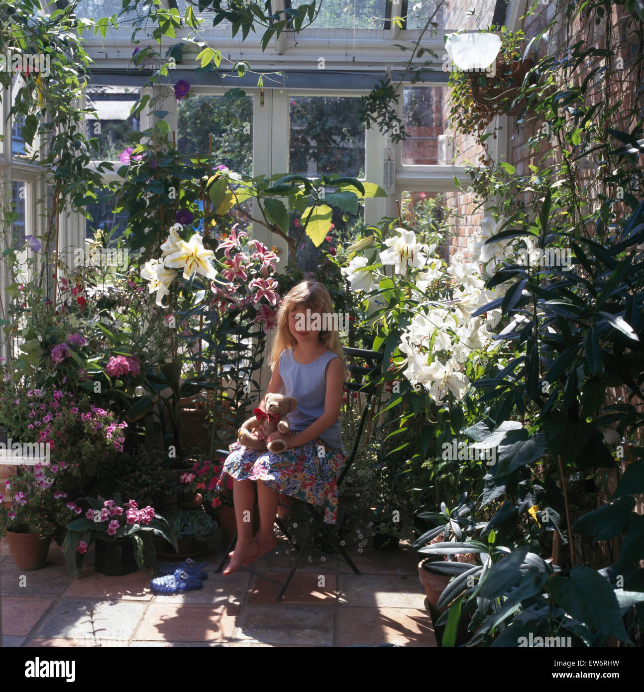 Petite fille assise dans une véranda plein de plantes à fleurs Banque D'Images