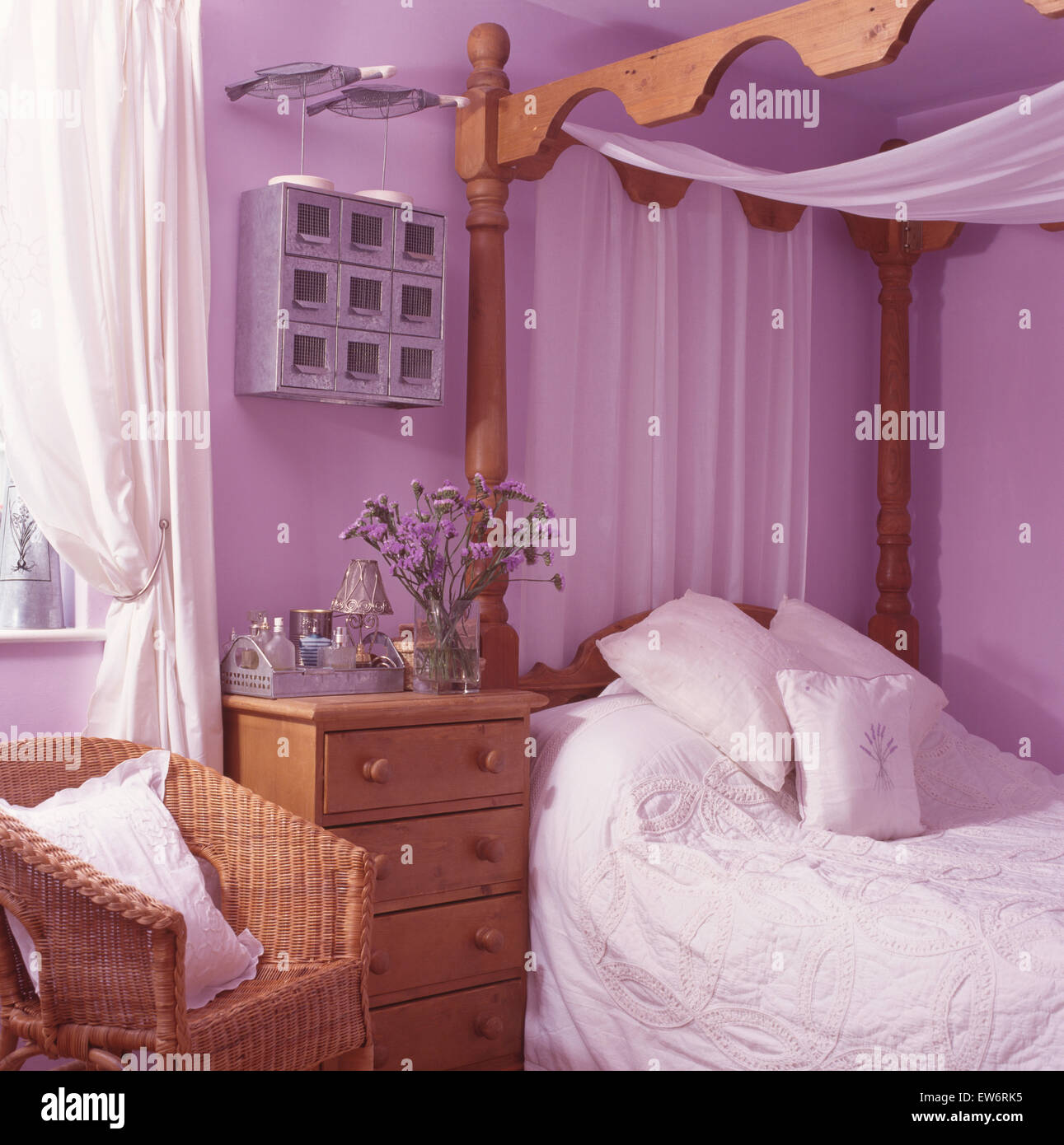 Rideaux voile blanc sur le pin lit baldaquin dans un mauve 90 chambre avec wicker chair Banque D'Images