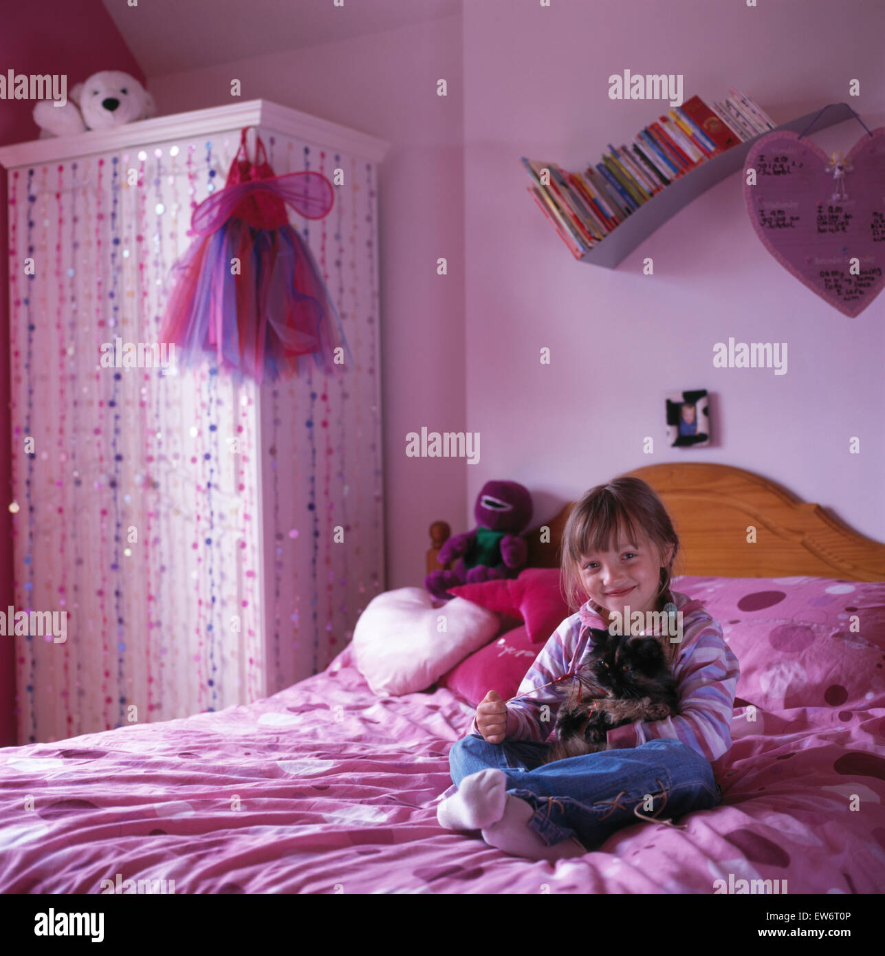 Petite fille assise sur le lit dans une chambre d'enfant années 90 rose Banque D'Images
