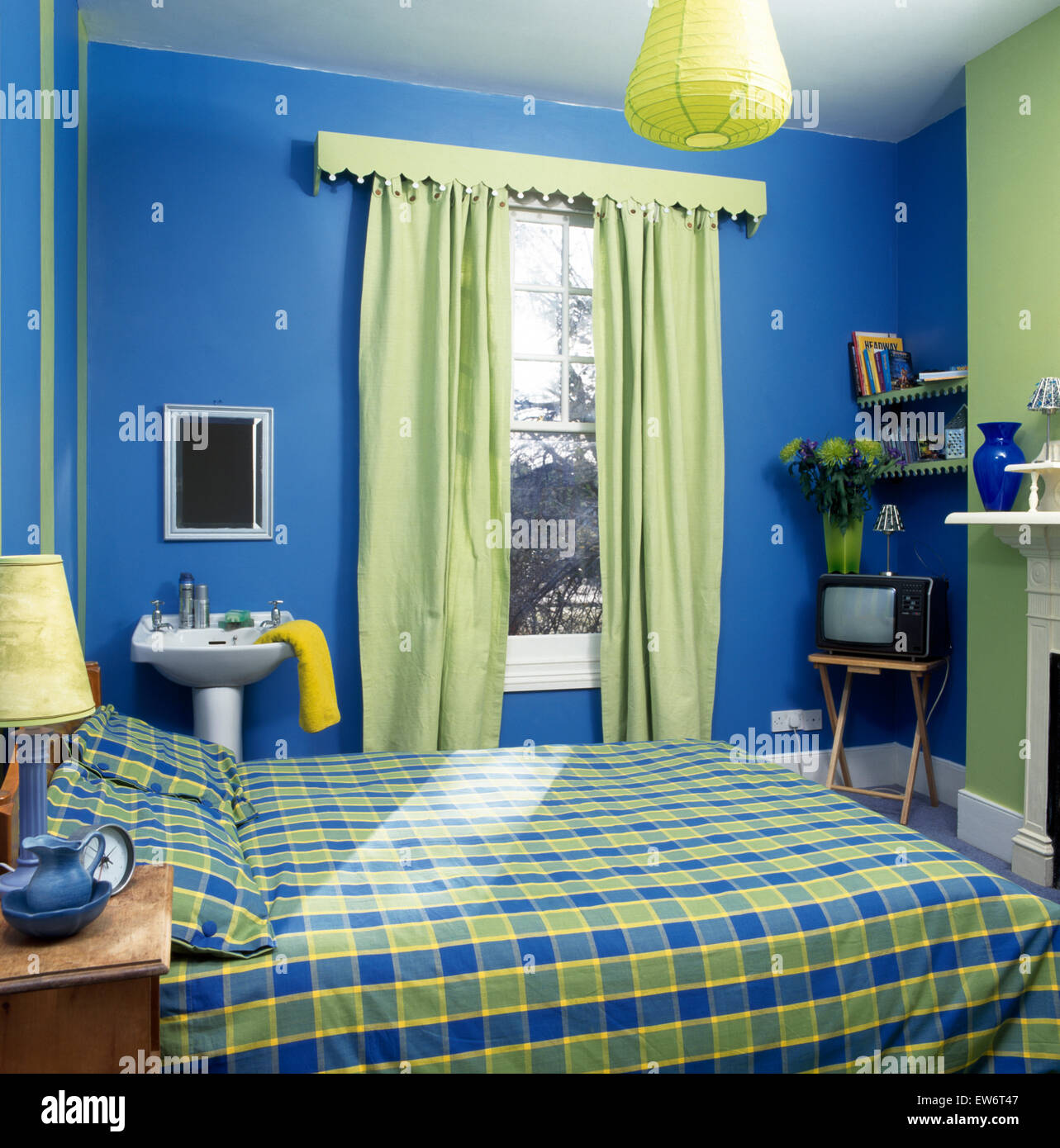 Vérifié sur couette lit dans l'économie des années 90 bleu chambre avec un piédestal vasque sur fenêtre avec rideaux verts Banque D'Images