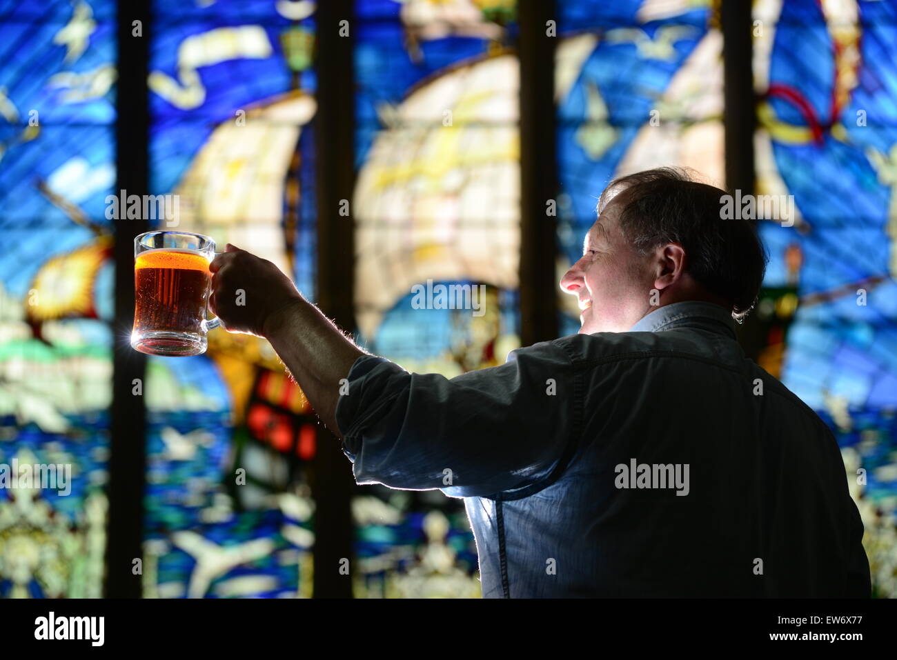 Un homme du levage d'une pinte d'ale en face d'un vitrail. Photo : Scott Bairstow/Alamy Banque D'Images