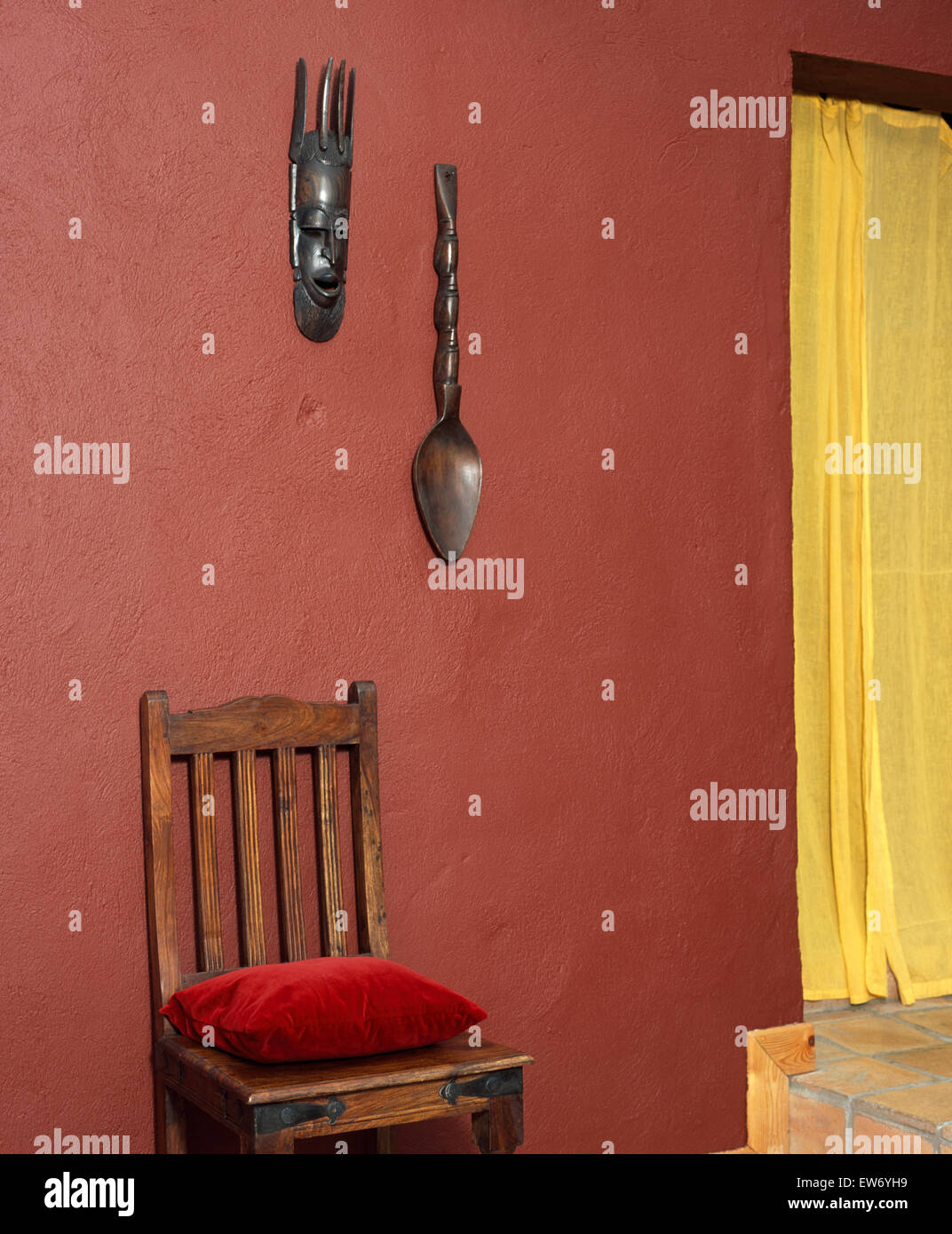 Masque de style africain et la cuillère sur le mur au-dessus de chaise en bois de base dans 90 ans avec des rideaux jaune Banque D'Images