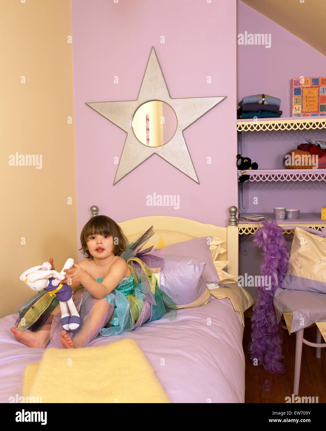 Portrait d'une petite fille portant un costume de fée assise sur le lit dans une chambre à thème star pour un usage éditorial uniquement Banque D'Images
