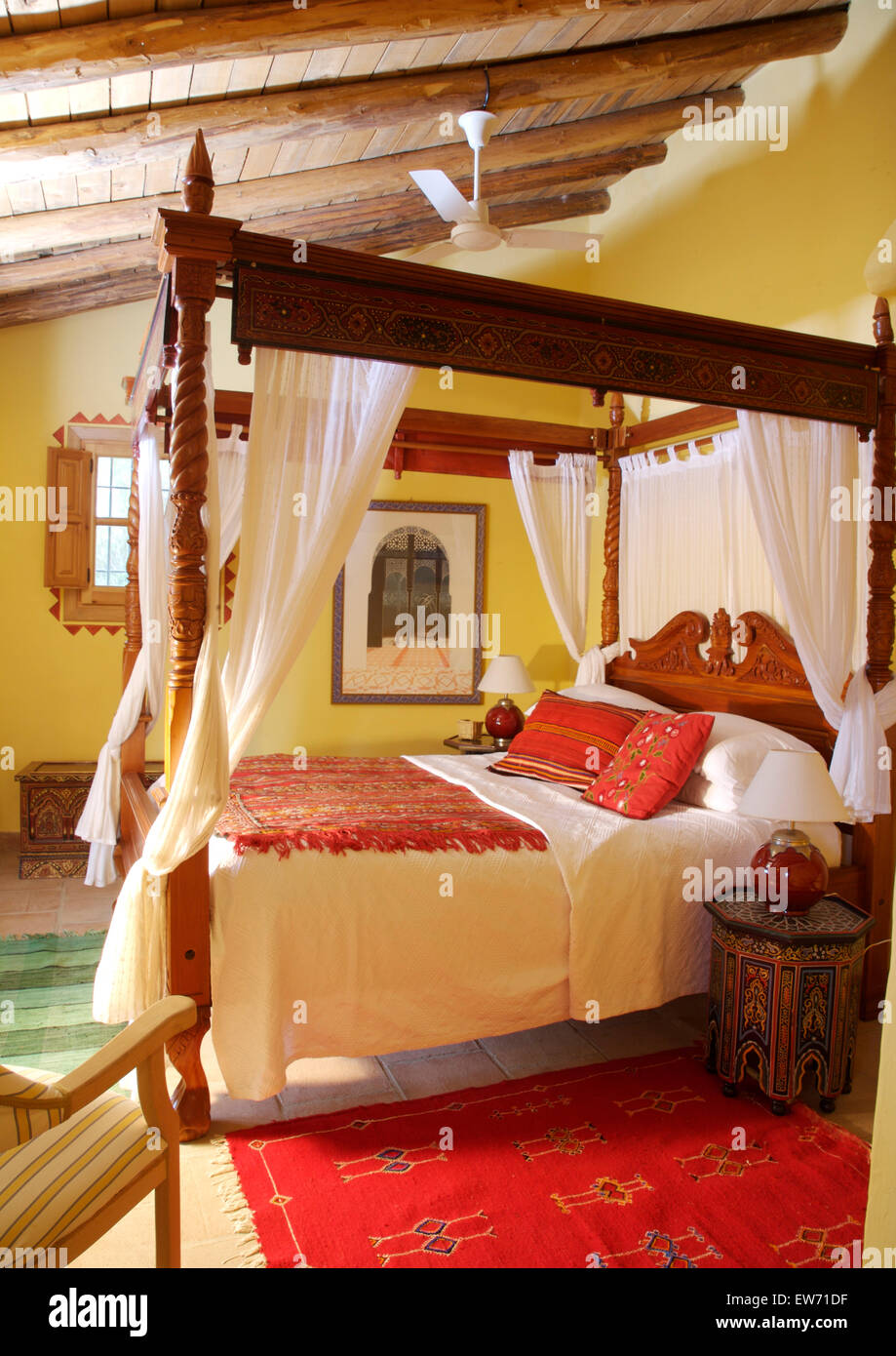 Coussins et tapis rouge ethnique sur lit à baldaquin en bois rustique avec  des rideaux blancs en jaune l'espagnol chambre pays Photo Stock - Alamy