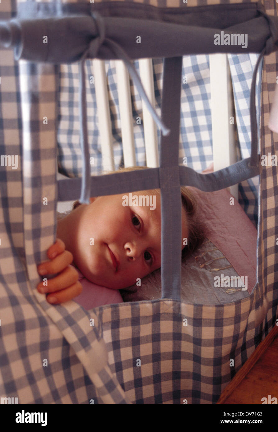 Close-up of a baby boy couché dans un lit avec des rideaux bleu vérifié Banque D'Images