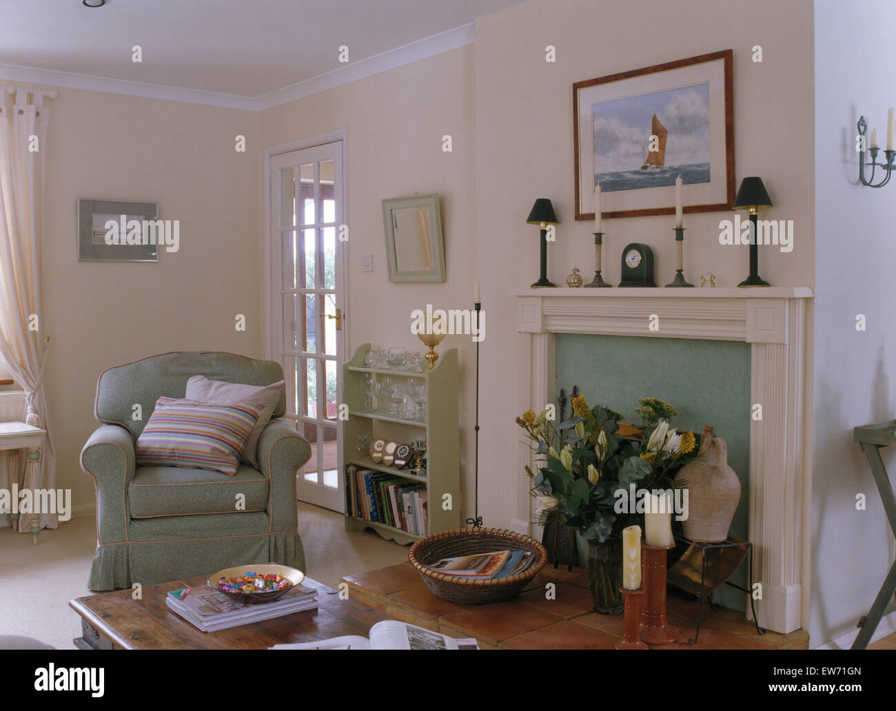 Vert sauge fauteuil et petite étagère à côté cheminée peinte en blanc pays salon Banque D'Images