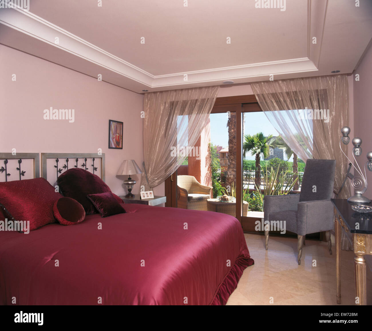 Couvre-lit en satin rose foncé sur le lit dans la chambre à coucher appartement espagnol avec rideaux d'organza sur portes de patio Banque D'Images