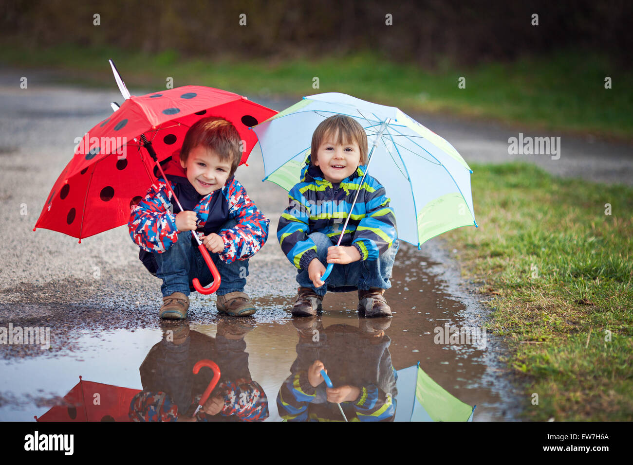 Deux petits garçons, l'accroupissement sur une flaque d'eau, avec peu de parasols Banque D'Images