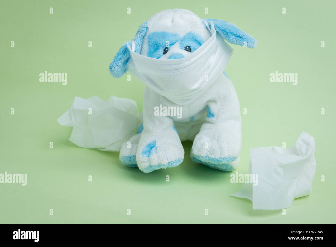 Un chien en peluche blanc et bleu portant un masque chirurgical entouré par les tissus utilisés représentant l'expression idiomatique 'Sick comme un chien Banque D'Images