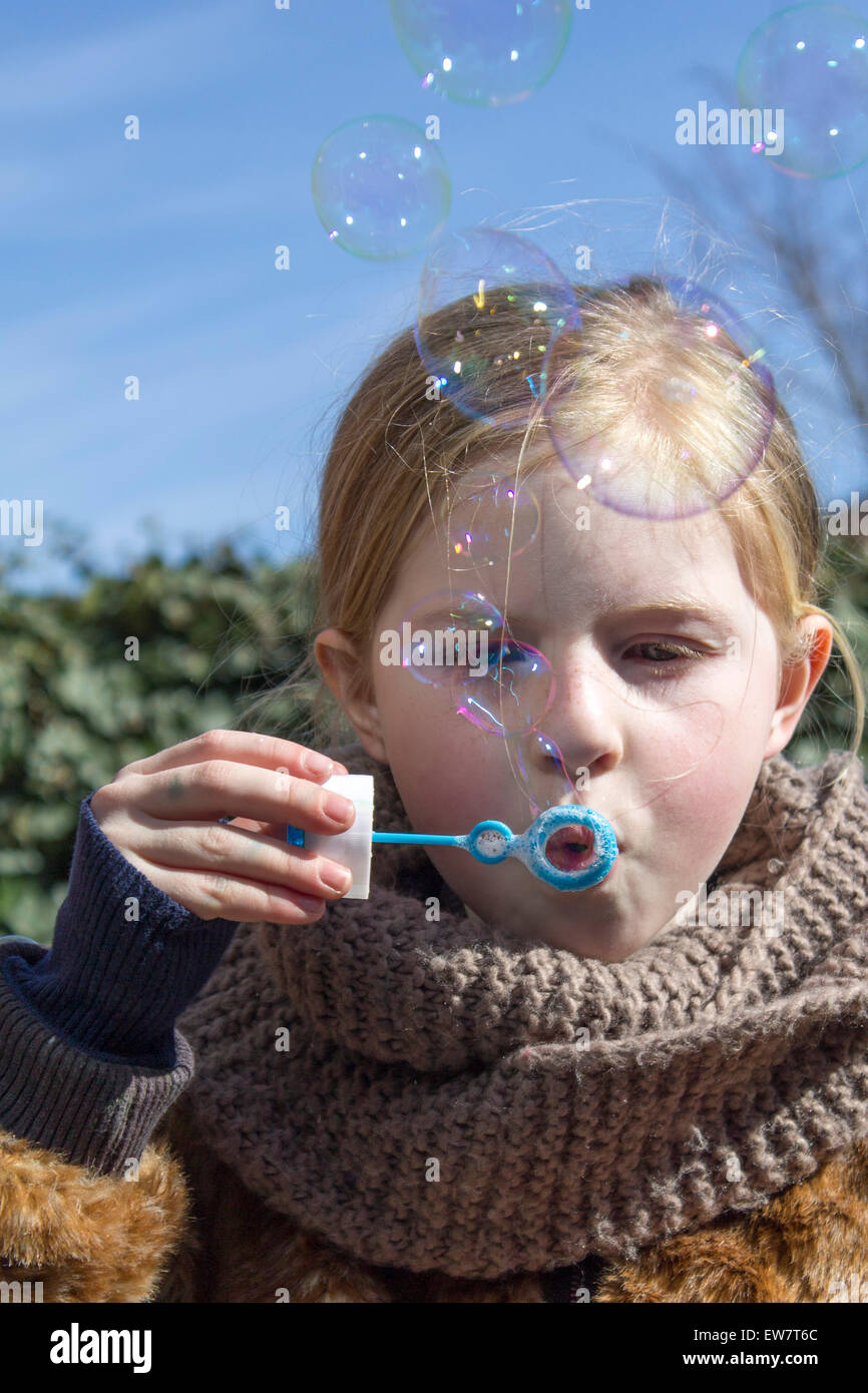 Fille debout dans le jardin bulles de savon soufflantes avec une baguette de bulle Banque D'Images