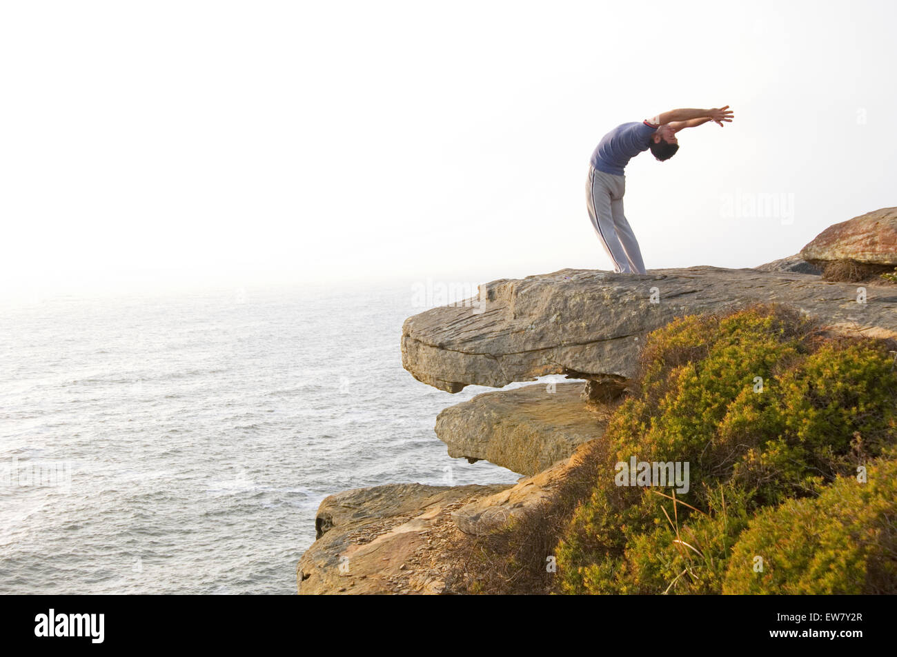 Un homme pratiquant le yoga sur un éperon rocheux au-dessus de l'océan Pacifique au nord, l'un de Curl Curl Sydneys Plages du Nord. Sy Banque D'Images