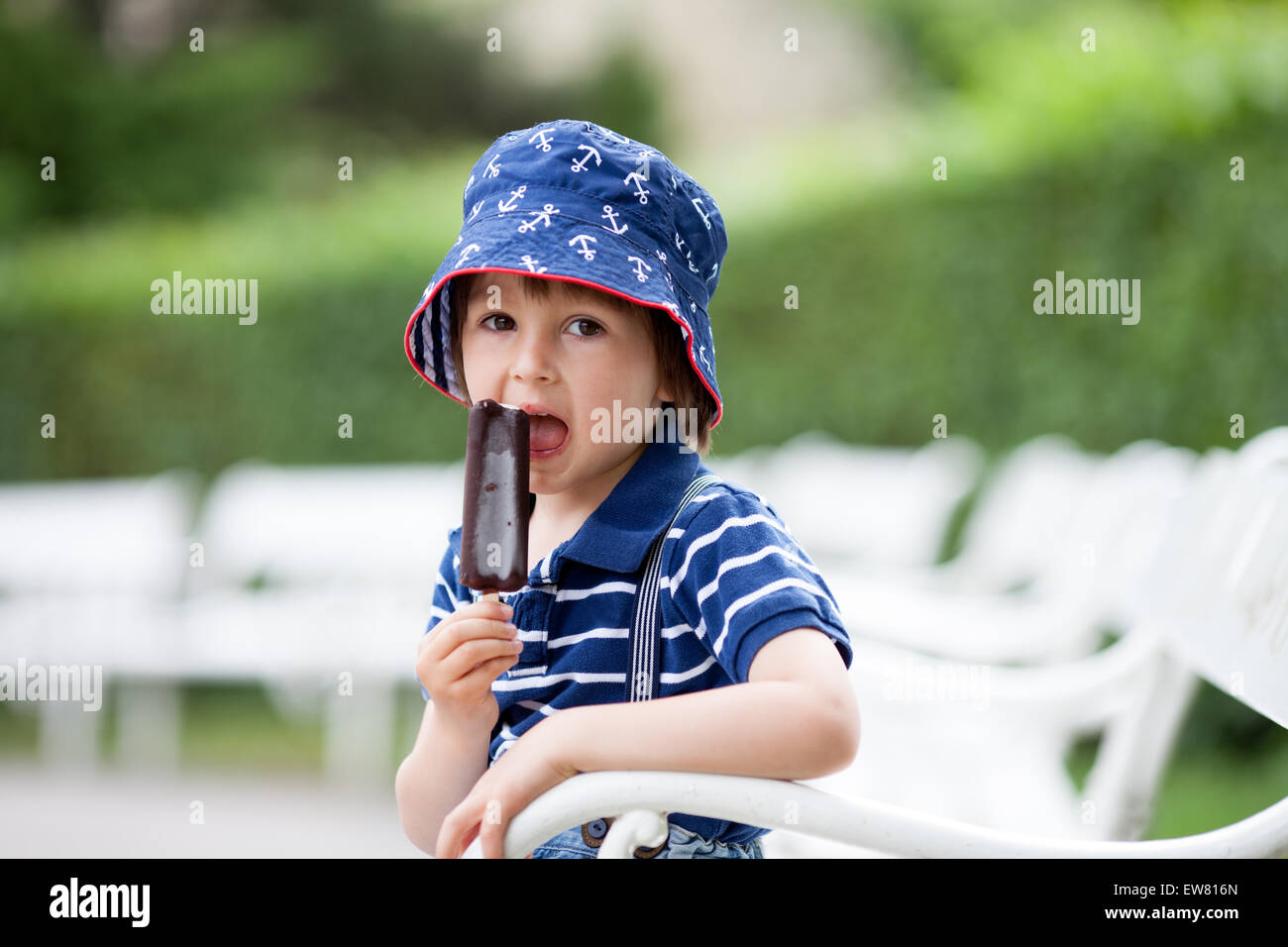 Happy little kid boy eating ice cream, extérieur, l'heure d'été, assis sur un banc blanc Banque D'Images