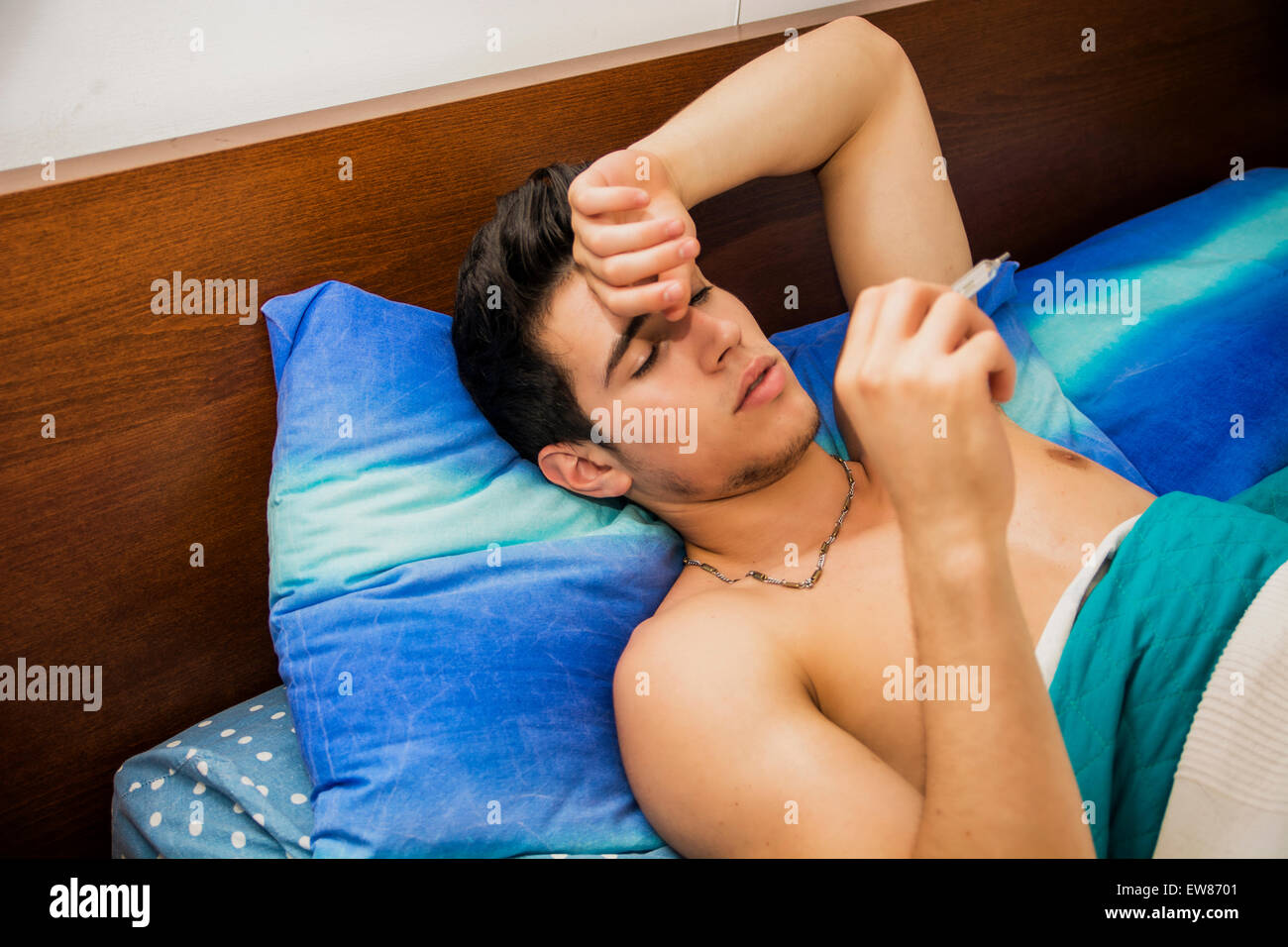 Jeune homme séduisant au lit avec une grippe ou une fièvre de mesure avec le thermomètre dans la bouche Banque D'Images