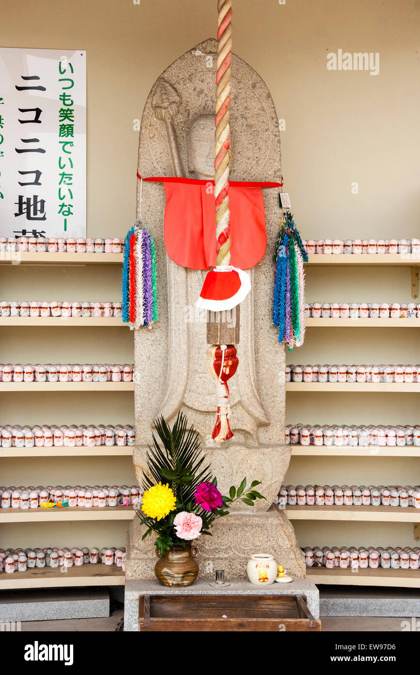 Grand Jizo japonais, alias Ojizo-sama, statue Jizo bosatsu, avec des centaines de minuscules derrière sur des supports à la temple Senkoji, Onomichi, le Japon. Banque D'Images