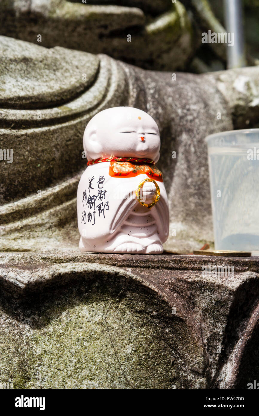 Le Japon, l'Onomichi, Temple Senkoji. Un petit Ojizo-sama, jizo Jizo bosatsu, figure avec dossard rouge, à gauche à la base d'une statue de l'un des dieux japonais. Banque D'Images