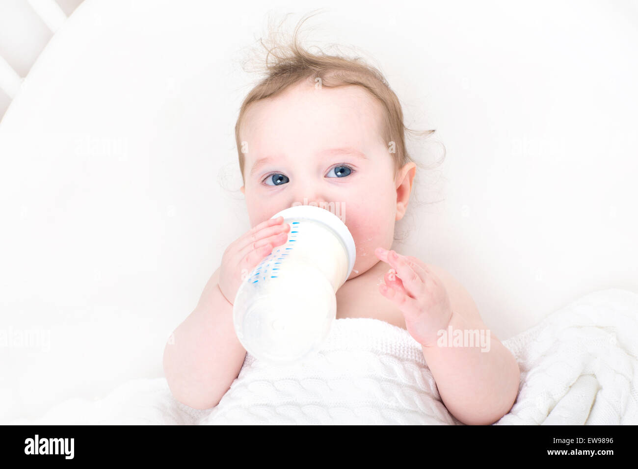 Petit bébé boire du lait à partir d'une bouteille dans un lit blanc Banque D'Images