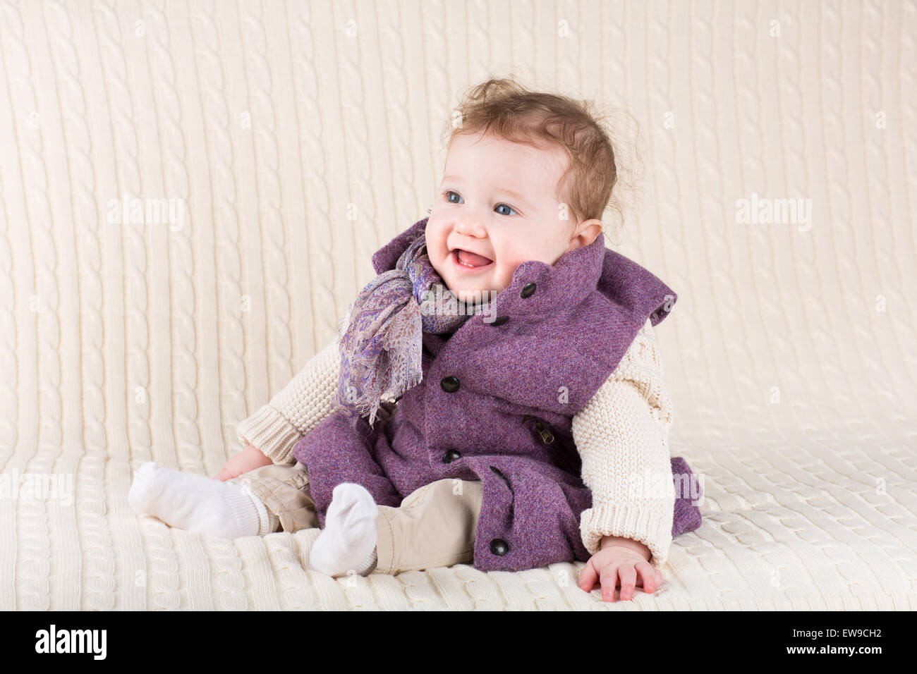 Laughing baby cute girl in a purple jacket assis sur une couverture en tricot Banque D'Images