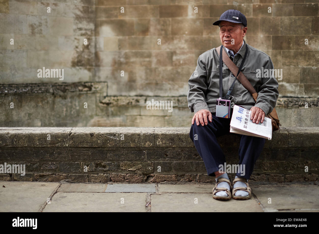 Un homme asiatique s'assoit sur un mur sur la rue Saint John's, à  Cambridge, avec un papier et une radio autour de son cou pour les  promenades guidées Photo Stock - Alamy