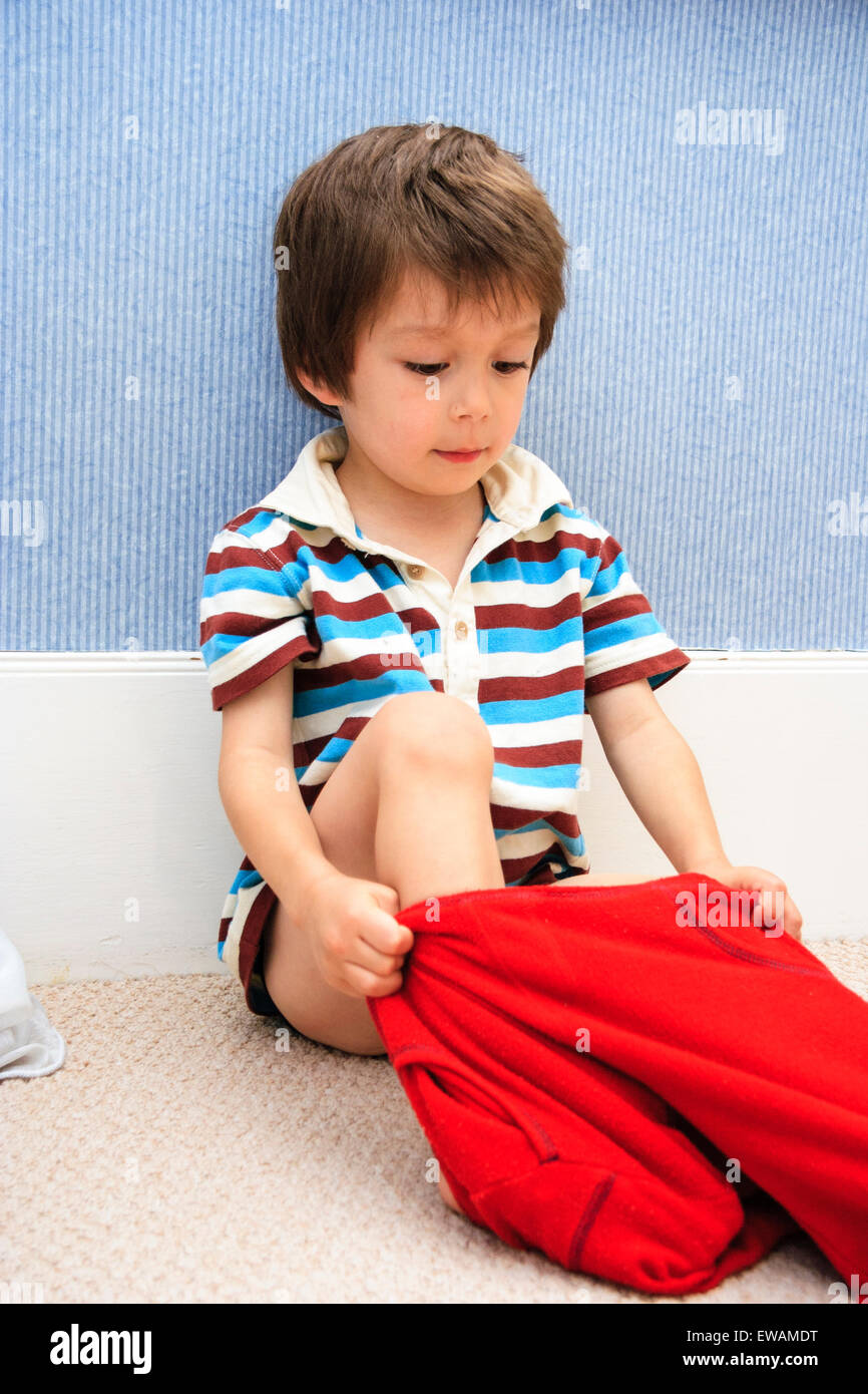 Caucasien enfant, garçon, 3-4 ans. À l'intérieur, assis sur un tapis contre  plinthe et le mur, tirant sur une paire de pantalon rouge Photo Stock -  Alamy