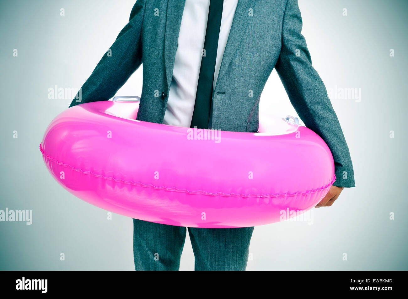 Un jeune homme de race blanche portant un costume gris avec un anneau de bain rose autour de sa taille, avec un léger vignettage ajouté Banque D'Images