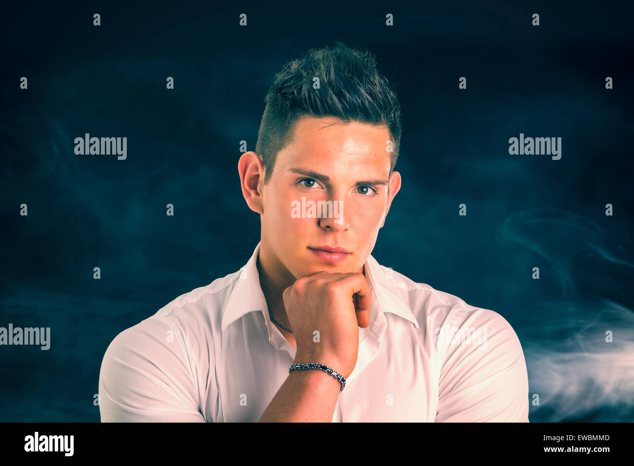 Tête et des épaules de beau jeune homme élégant avec chemise, looking at camera, sur fond sombre Banque D'Images