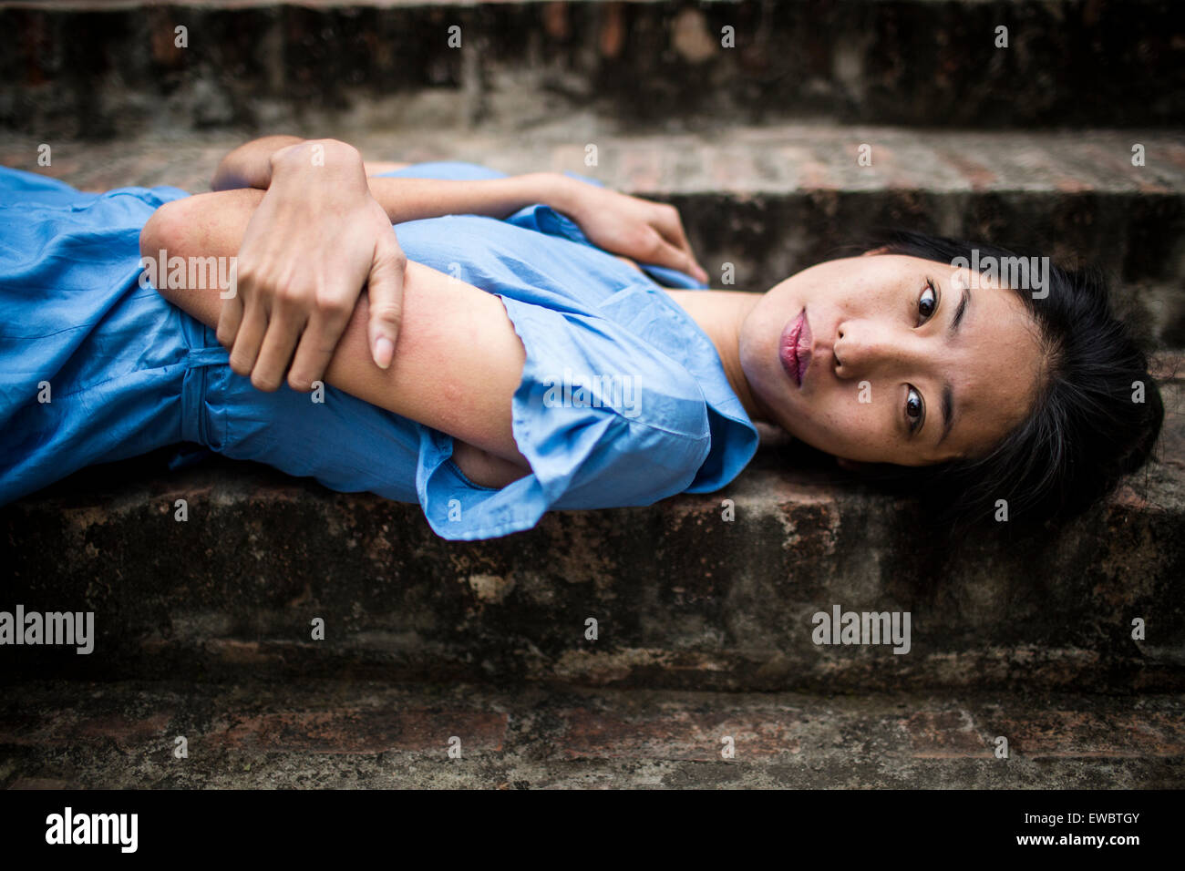 Une jeune vietnamienne dans une robe bleue, couché sur des marches en pierre dans les régions rurales de Hanoi, Vietnam. Banque D'Images