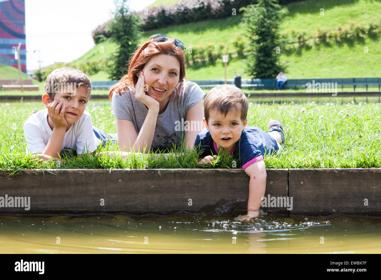 Portrait de mère de deux enfants allongés sur l'herbe sur la berge d'un étang Banque D'Images