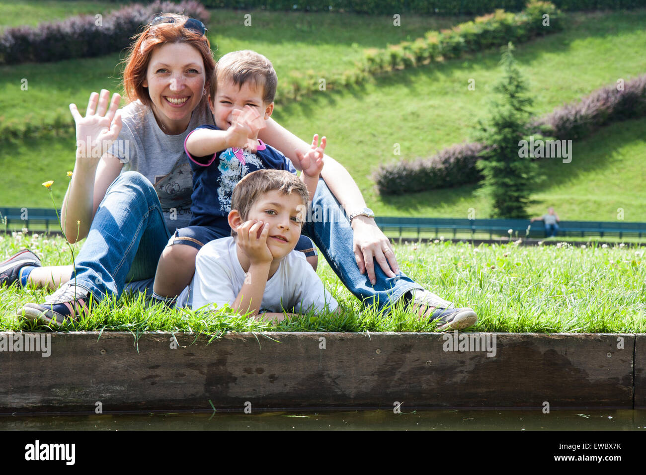 Portrait de mère de deux enfants allongés sur l'herbe sur la berge d'un étang Banque D'Images