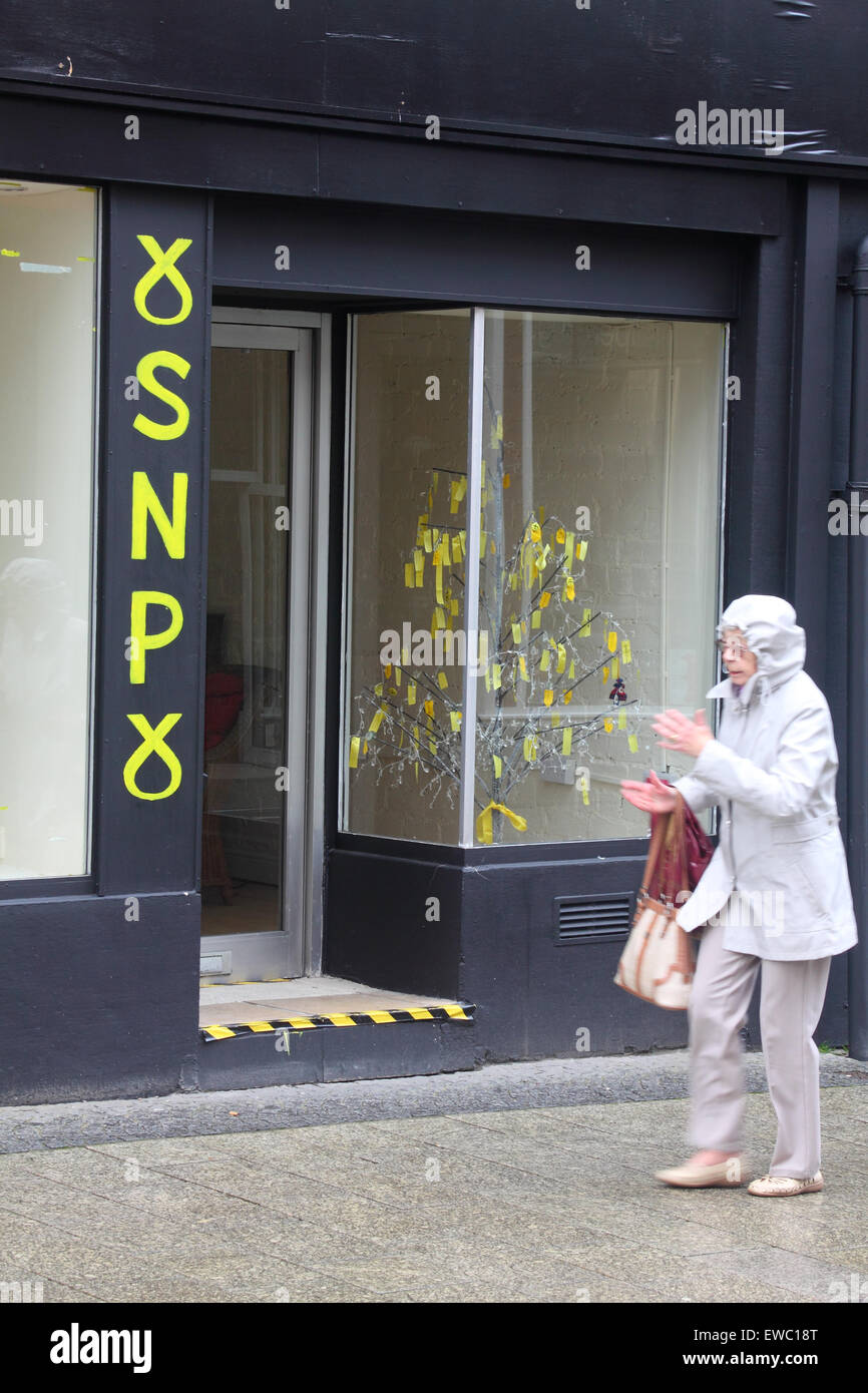 Femme âgée lors d'une journée pluvieuse à pied par le SNP bureau à Fort William, Écosse. Banque D'Images