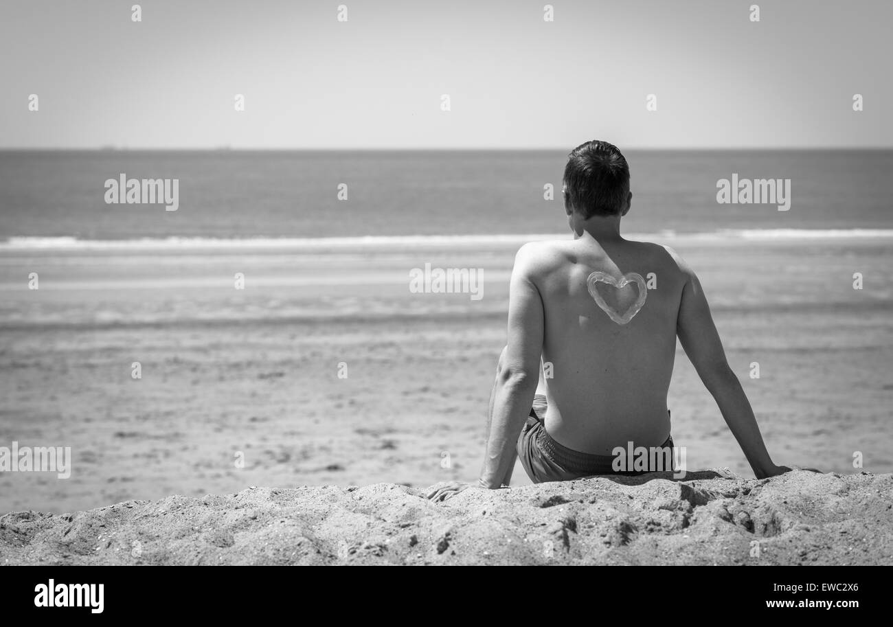 L'homme assis sur la plage et vous détendre avec un coeur sur le dos Banque D'Images