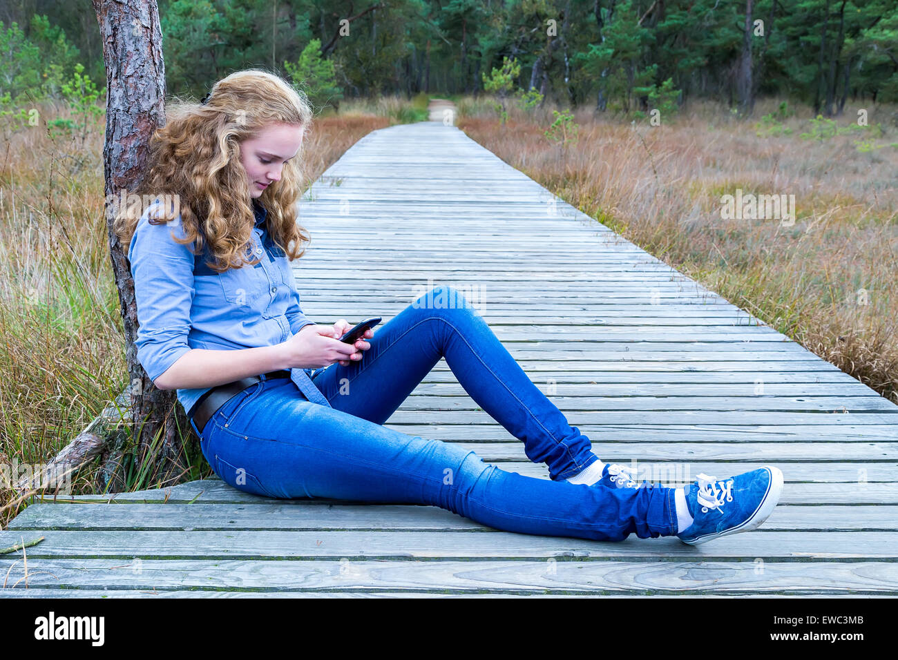 Portrait of teenage girl sitting on wooden sentier dans la nature mobile téléphone Banque D'Images