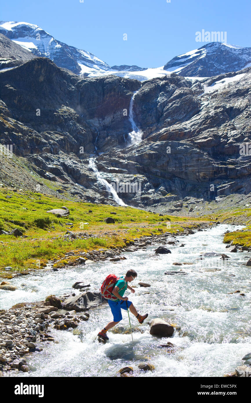 Un male hiker sautant de pierre en pierre pour traverser une rivière, au cours de l'étape 7 Glocknerrunde, un trekking de Kaprun à Kals Banque D'Images