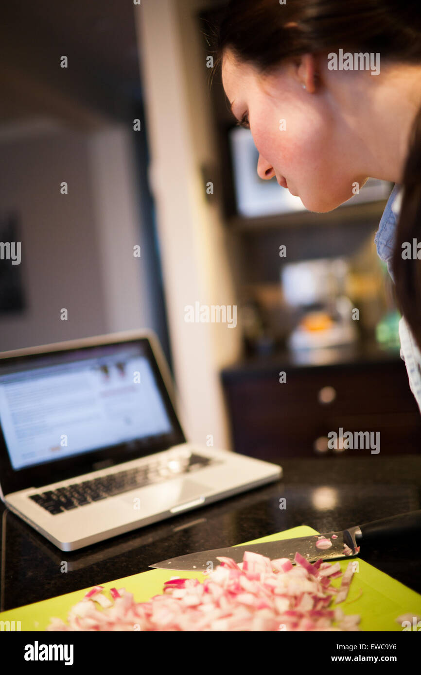 Une jeune femme lit une recette de son ordinateur portable. Banque D'Images