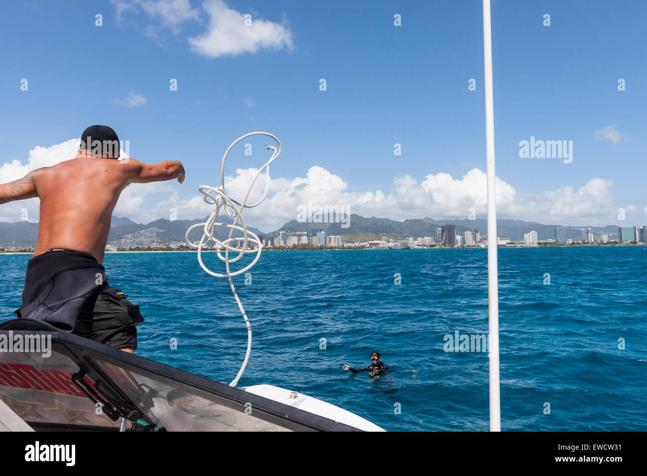 Un homme jette une corde à un plongeur d'ancrer un bateau de plongée à une amarre de ballon sur la plage de Waikiki à plonger. Banque D'Images