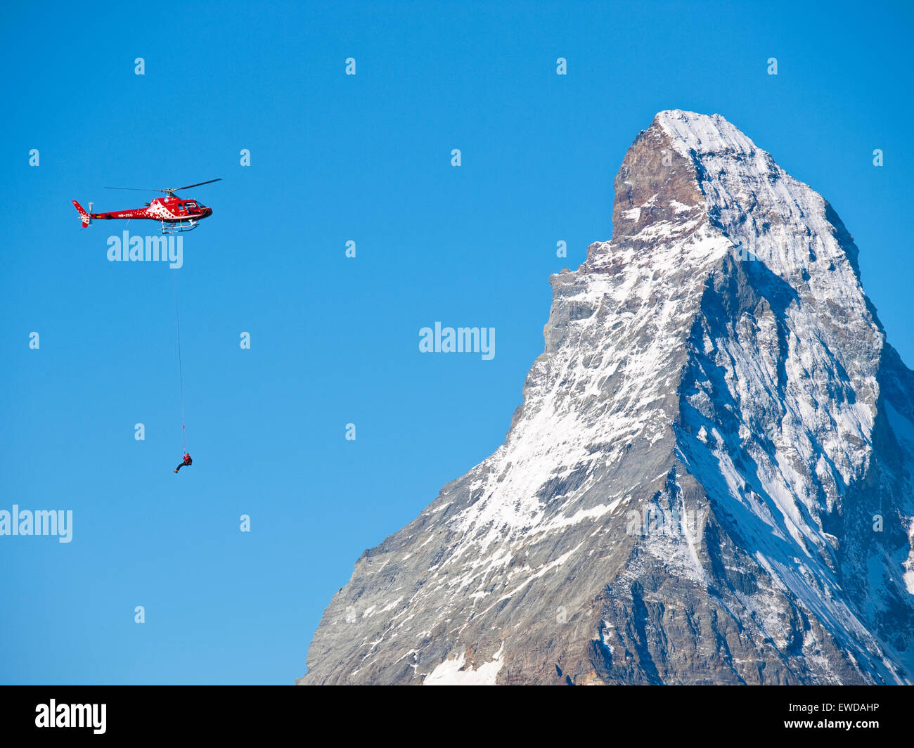 Un technicien de sauvetage en montagne pend au-dessous d'un hélicoptère pendant une mission de sauvetage d'un alpiniste blessé dans les Alpes suisses. Banque D'Images