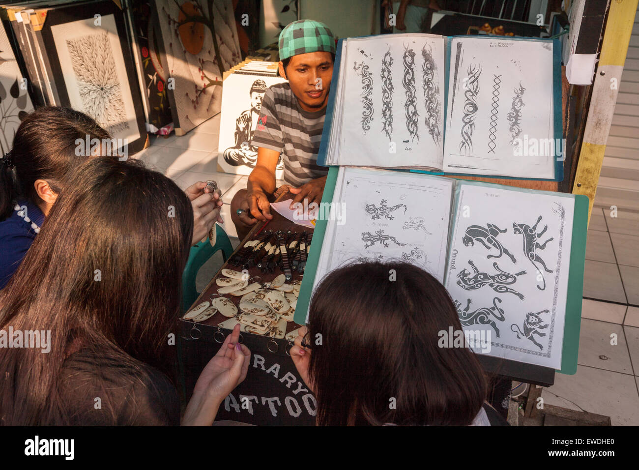 Un shopper attend alors qu'un groupe de femmes touristes discutent d'options tout en se croquant devant un grand livre de présentation de tatouage à Bali. Banque D'Images