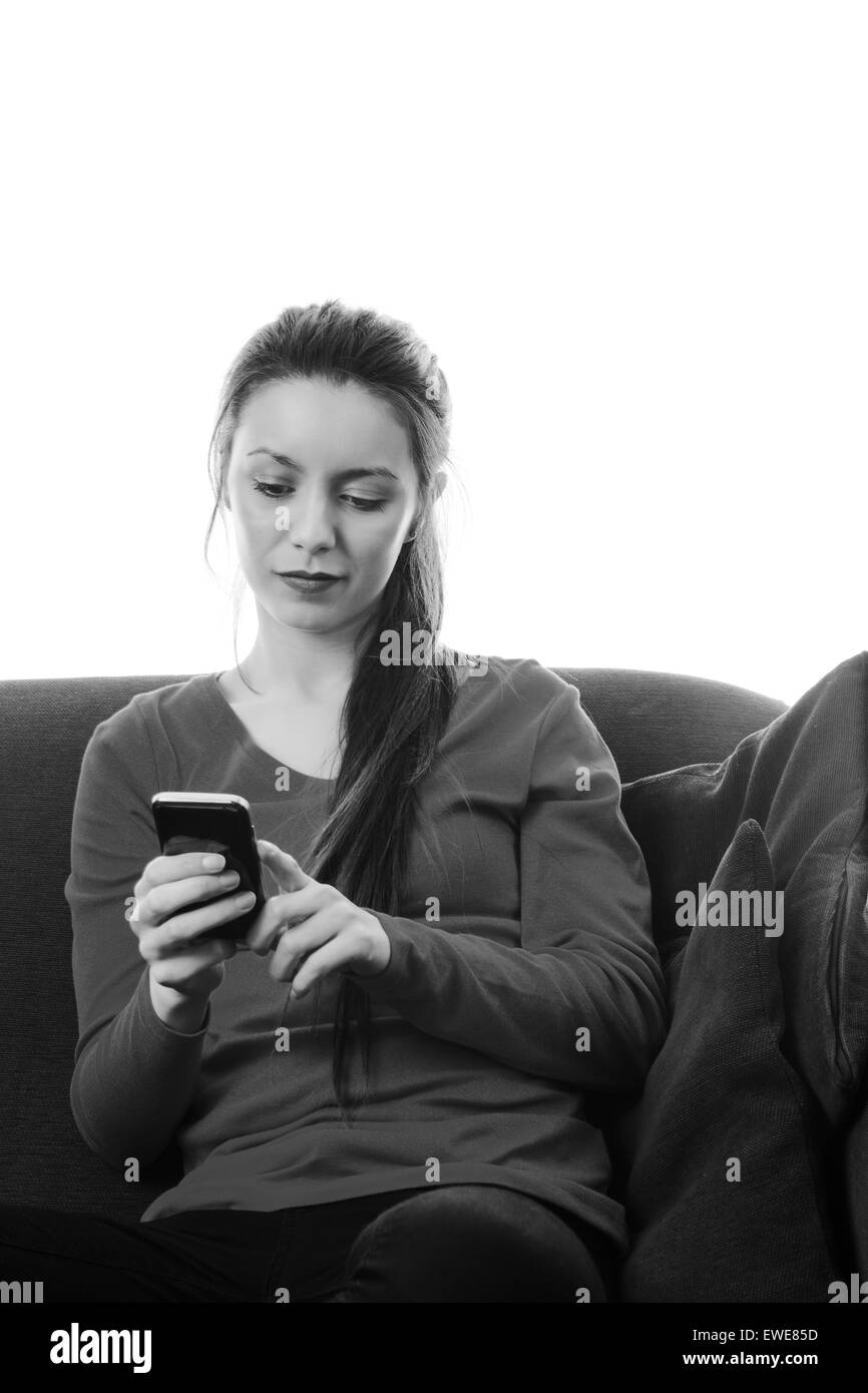 Femme assise sur un canapé des sms sur un téléphone mobile Banque D'Images